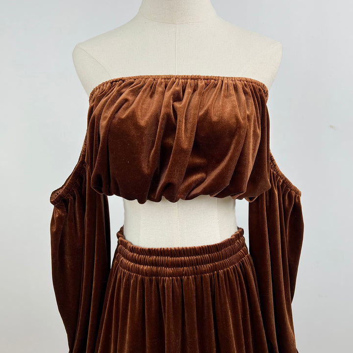 A mannequin displays a close-up of Belisama dress velvet off-shoulder top and floor-length skirt. The two-piece outfit has a ruffled skirt hem.