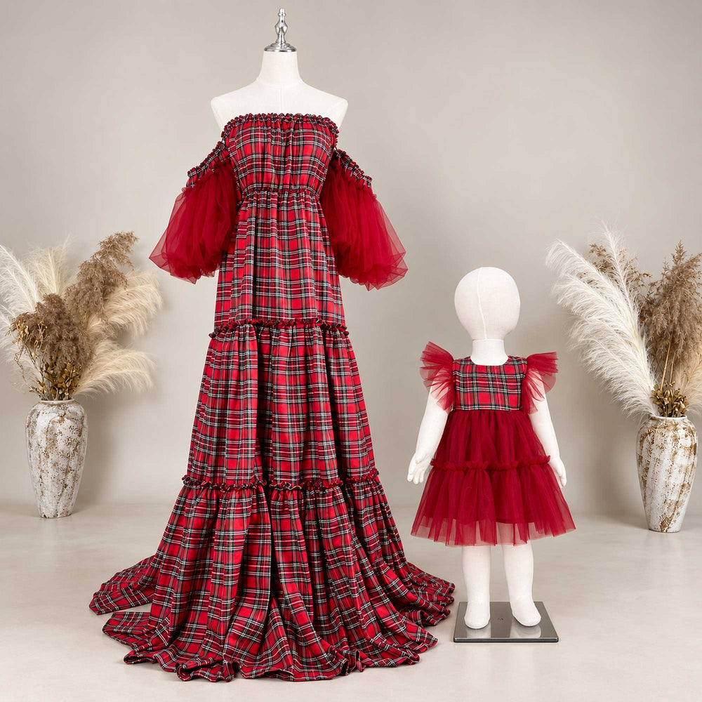 An adult maxi dress and a toddler dress on two mannequins of different sizes, both in red-black plaid with red tulle, a dried-flower vase on each side.