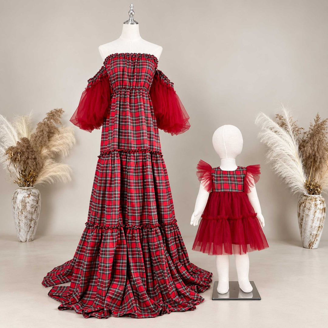 An adult maxi dress and a toddler dress on two mannequins of different sizes, both in red-black plaid with red tulle, a dried-flower vase on each side.