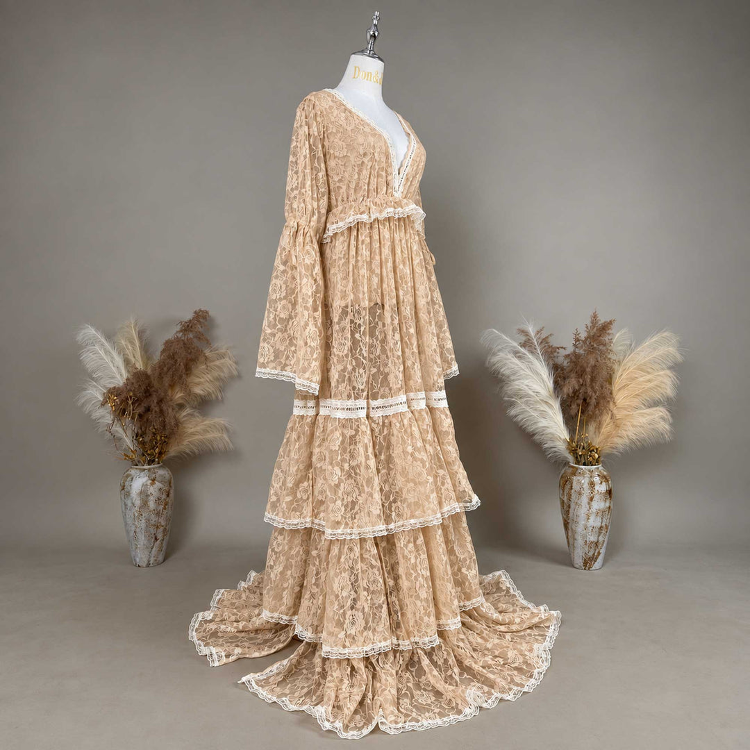 A Clito khaki lace long-sleeve dress on a mannequin from an oblique angle, tiered skirt, train on the floor, a dried-flower vase on each side.
