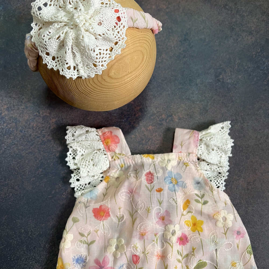 A close-up of the upper part of the same romper, showing both straps, the crochet lace and the embroidered floral fabric, with the headband partly visible above.