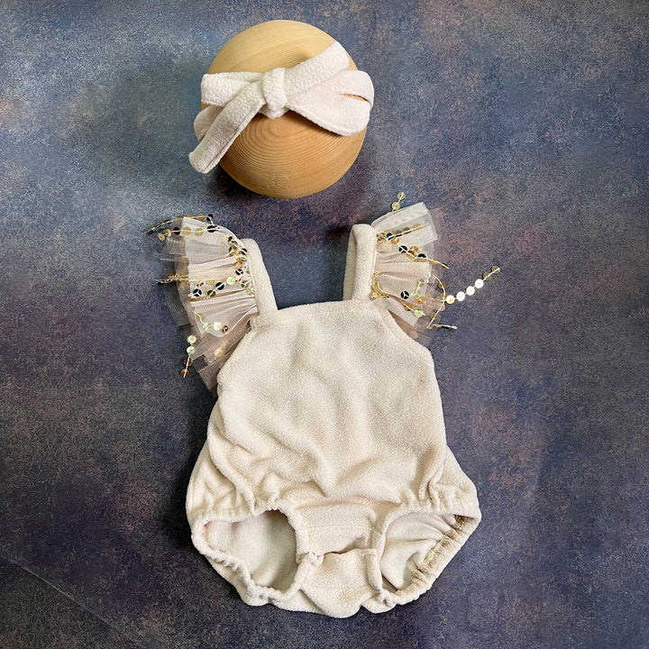 A romper laid flat from the front, showing the square neckline, tulle sequin straps on both sides and gathered leg openings, with the same bow headband above.