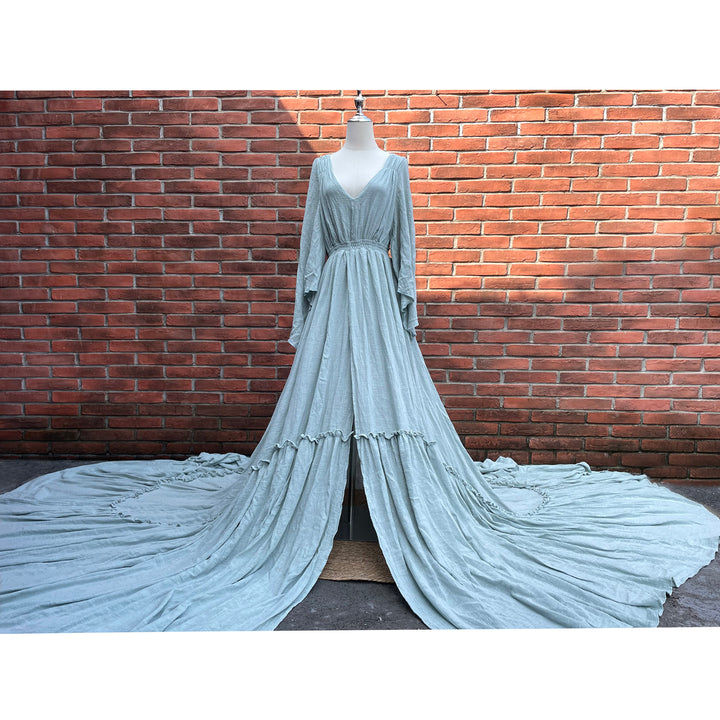 A light blue Daphne long-sleeved V-neck gown is displayed on a mannequin.The dress features a high front slit and its hem and train are spread out on the wooden floor.