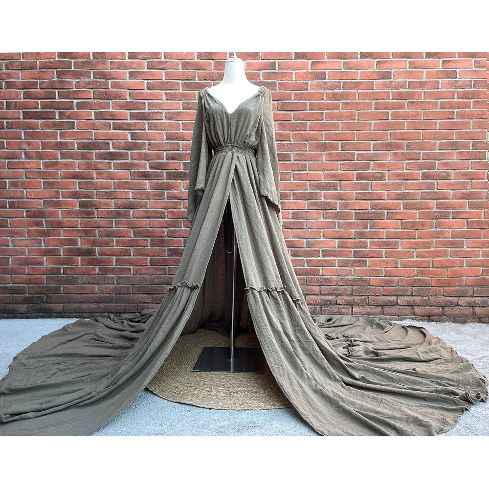 A Daphne olive long-sleeved V-neck gown is displayed on a mannequin. The dress features a high front slit and its hem and train are spread out on the wooden floor.