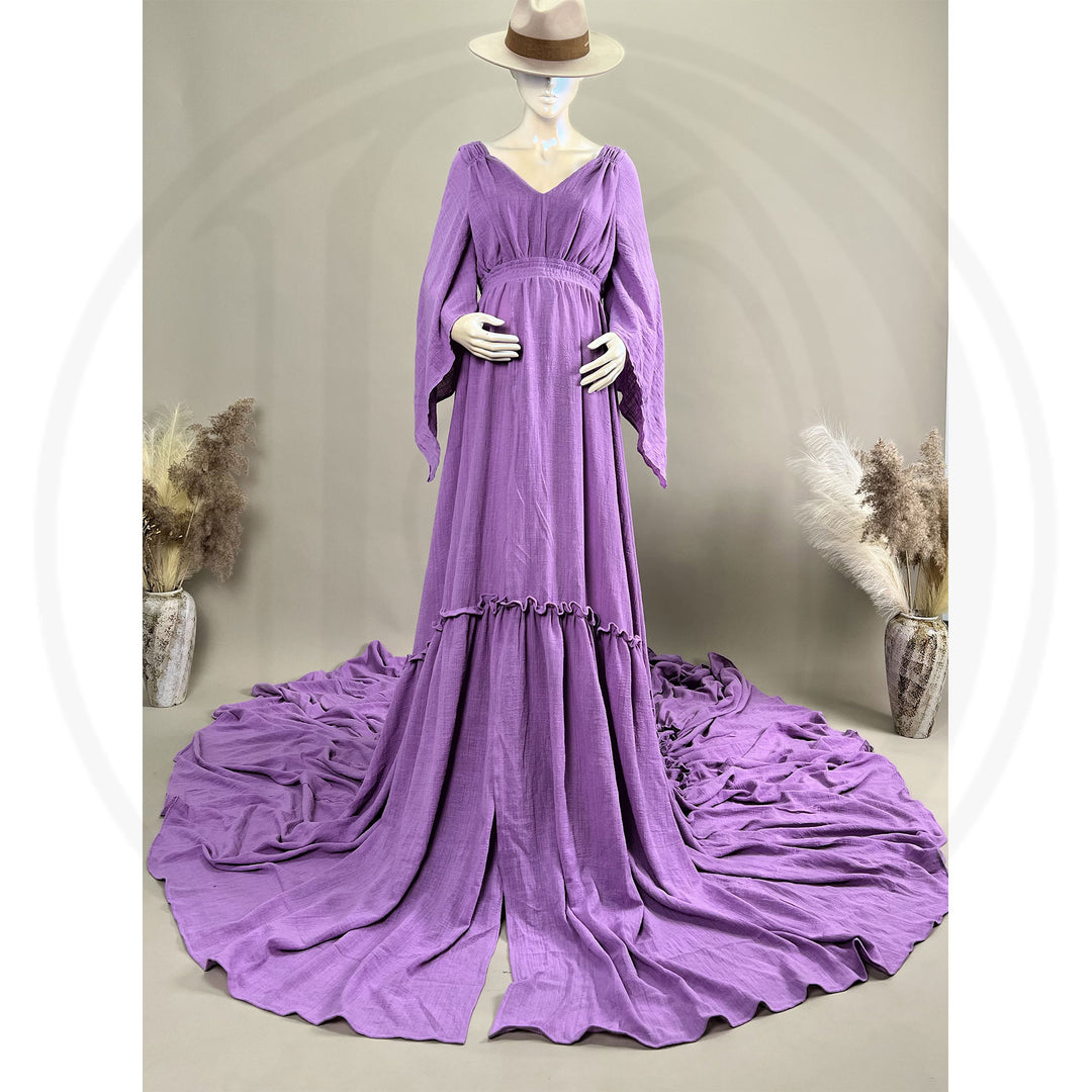 A Daphne lavender long-sleeved V-neck gown is displayed on a mannequin, with hands positioned on the simulated belly. The dress features a high front slit and its hem and train are spread out on the wooden floor.