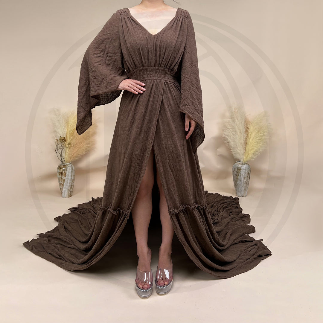 A Daphne coffee long-sleeved V-neck gown is displayed on a mannequin. The dress features a high front slit and its hem and train are spread out on the wooden floor.