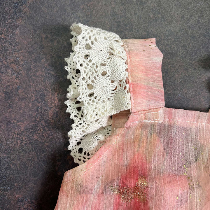 A close-up of the same romper, showing one white crochet lace piece, the shoulder-strap stitching and the pink fabric with gold specks.