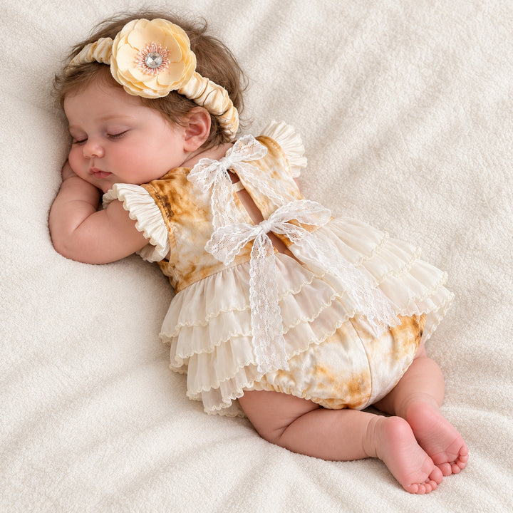 A baby lying on her side, showing the lace ribbon bow on the back and the tiered skirt, head resting on her arm.